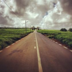 Road passing through field against cloudy sky