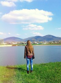 Rear view of woman standing by lake against sky