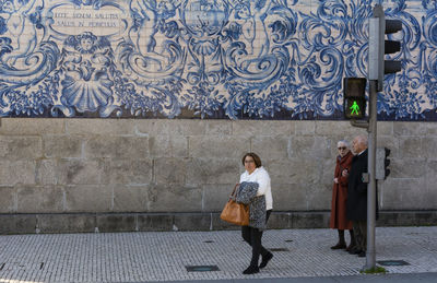 Full length of woman walking on footpath against wall