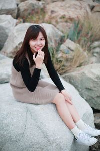 Portrait of smiling young woman sitting on rock at beach