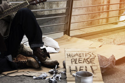 Low section of homeless man sitting by railing