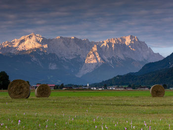 Hay bales on field by mountains against sky