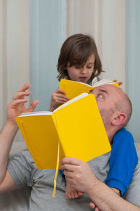 Father and son together enjoying reading and discussing school homework from yellow textbook.