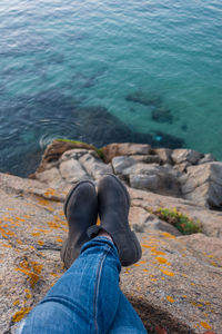 Low section of woman sitting on rock against sea