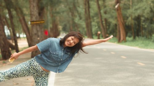 Young woman with arms raised on road against trees