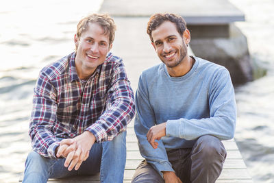 Portrait of happy male friends sitting on pier