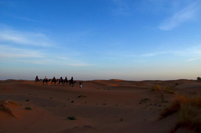 People on sand dune against sky