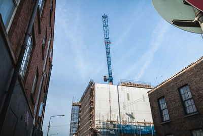 Low angle view of crane by buildings against sky