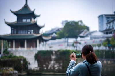 Rear view of woman photographing building in city