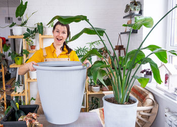 Portrait of smiling young woman holding potted plant on table