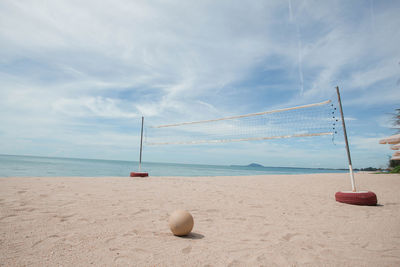 Net at beach against cloudy sky during sunny day