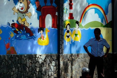 Rear view of man standing against graffiti wall