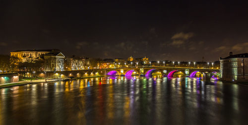 Illuminated bridge over river in city against sky at night