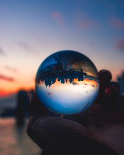 Close-up of hand holding crystal ball against sky during sunset