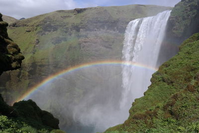 Scenic view of waterfall against rainbow in sky