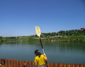 Rear view of girl with oar standing by lake