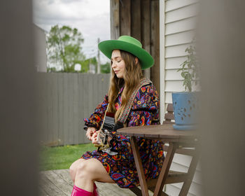 Side-view of a woman with eyes closed sitting on porch playing guitar