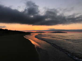 Scenic view of beach against dramatic sky during sunset