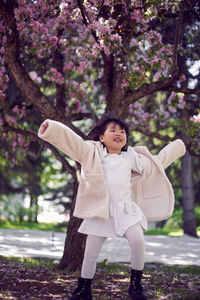 Korean girl in a white light fur coat and a headband run in a garden with cherry blossoms
