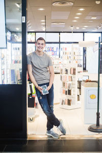 Full length portrait of smiling young salesman holding phone cover while standing at store entrance