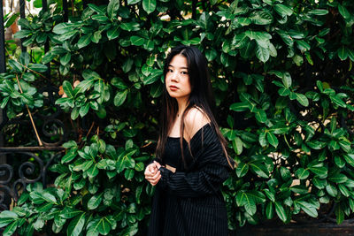 Portrait of beautiful young woman standing against plants