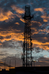 Low angle view of silhouette communications tower against cloudy sky during sunset