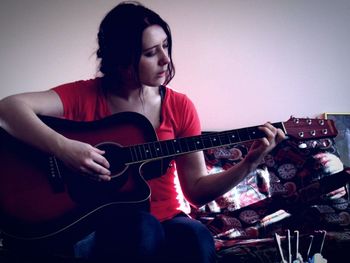 Woman playing guitar while sitting on sofa at home