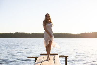 Beautiful girl dressed in a white dress, walking along a wooden pier on the bank of a river or  lake