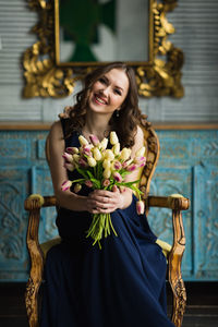 Portrait of smiling young woman holding flowers while sitting on chair