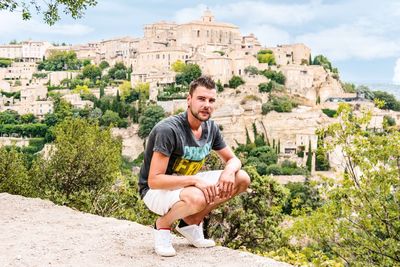 Portrait of young man crouching against village at gordes