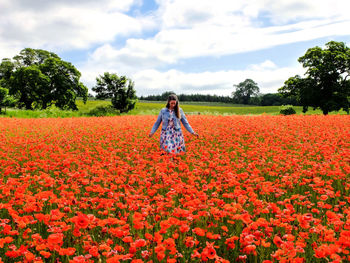 Woman on red flowering plants on field against sky