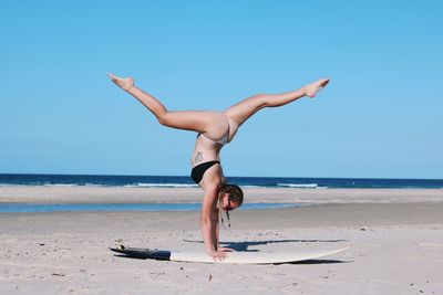 Woman doing handstand at beach against clear sky