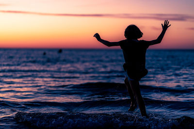 Rear view of silhouette man standing at beach during sunset