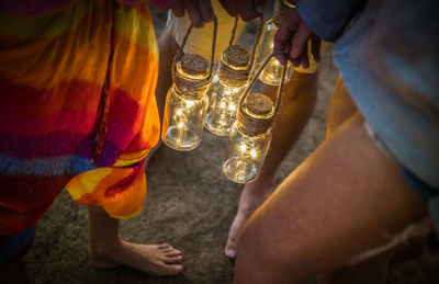 Low section of friends holding illuminated lighting equipment at beach