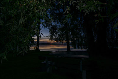 Empty park bench by trees against sky at night