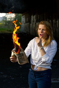 Young woman holding burning paper outdoors