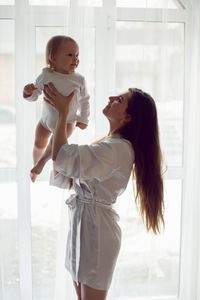 Mother in a white robe stands and up with a child a blonde daughter large window of the house person