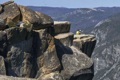 Rear view of man climbing on rock against sky