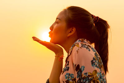 Optical illusion of woman blowing sun against clear sky during sunset