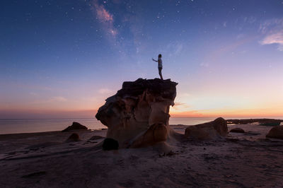 Man standing on rock at beach during sunset