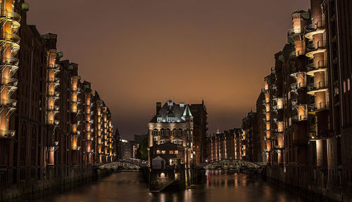 Low angle view of buildings in front of canal against sky at night