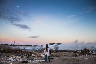 Woman standing on shore at sunset