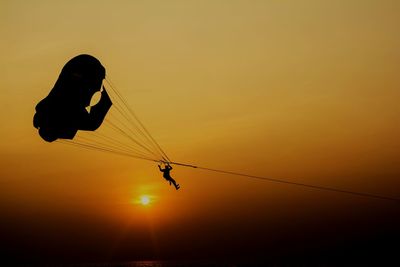 Silhouette person paragliding against clear sky during sunset