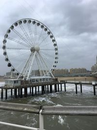 Ferris wheel by river against sky in winter