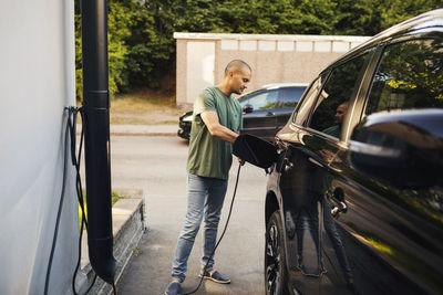 Man charging electric car by house