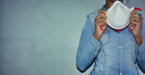 Midsection of woman holding mask against wall