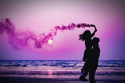 Silhouette couple with purple distress flare at beach during sunset