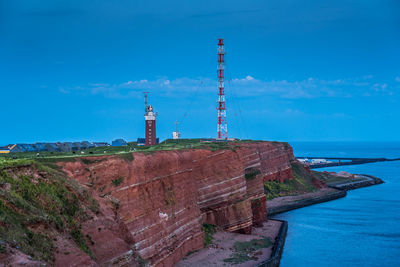 Lighthouse amidst sea and buildings against blue sky