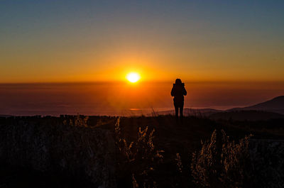 Silhouette man walking on landscape against sky during sunset