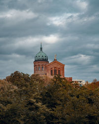 Low angle view of trees and church against cloudy sky